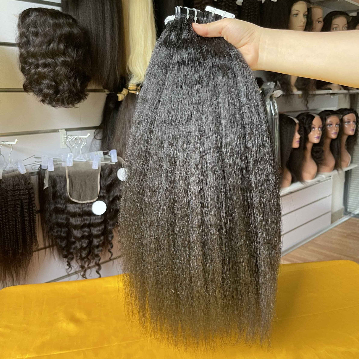 QWB Kinky Straight Tape-In Extension close-up detail shot highlighting distinctive steam-processed texture on individual weft strip approximately 2 inches wide. Natural #1b black Brazilian virgin human hair with cuticle intact showing subtle small braided/coiled pattern created by high temperature t