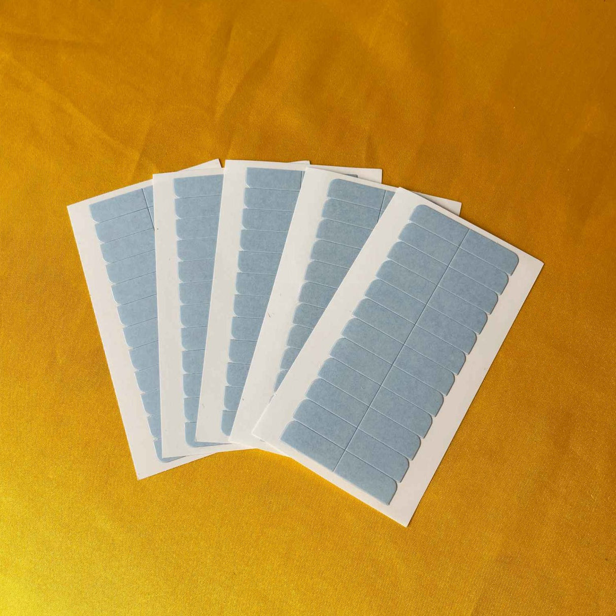 Adhesive Blue Tape Double-Sided For Tape-In Extension complete sheet display showing 12 individual adhesive strips arranged in organized grid pattern on protective backing paper. Each strip measures approximately 2 inches wide by length matching tape-in weft dimensions for full-width coverage ensuri